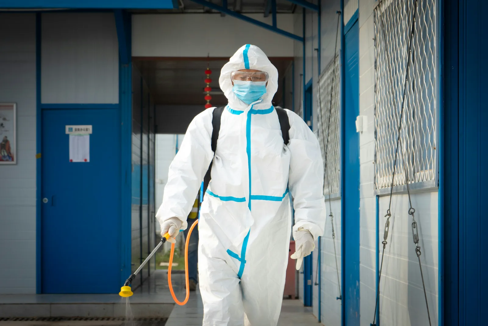 Mitarbeiter in Schutzanzug mit Sprühgerät bei der Desinfektion