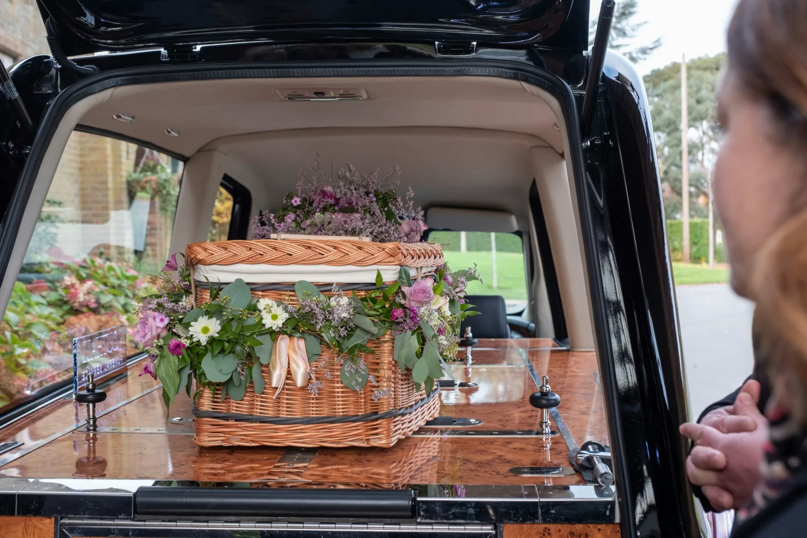 Blumengeschmückter Sarg in einem Bestattungsfahrzeug, Angehörige nehmen Abschied
